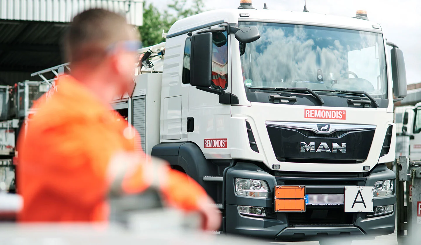 Un veicolo speciale per la raccolta dei rifiuti di REMONDIS e, davanti ad esso, un dipendente in abbigliamento da lavoro arancione ad alta visibilità.