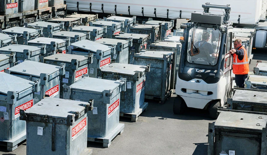 Area esterna con molti contenitori speciali per i rifiuti. Un dipendente parla con un altro collega seduto su un carrello elevatore.